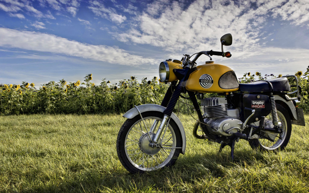 Gelbes Motorrad vor blauem Himmel und grüner Wiese
